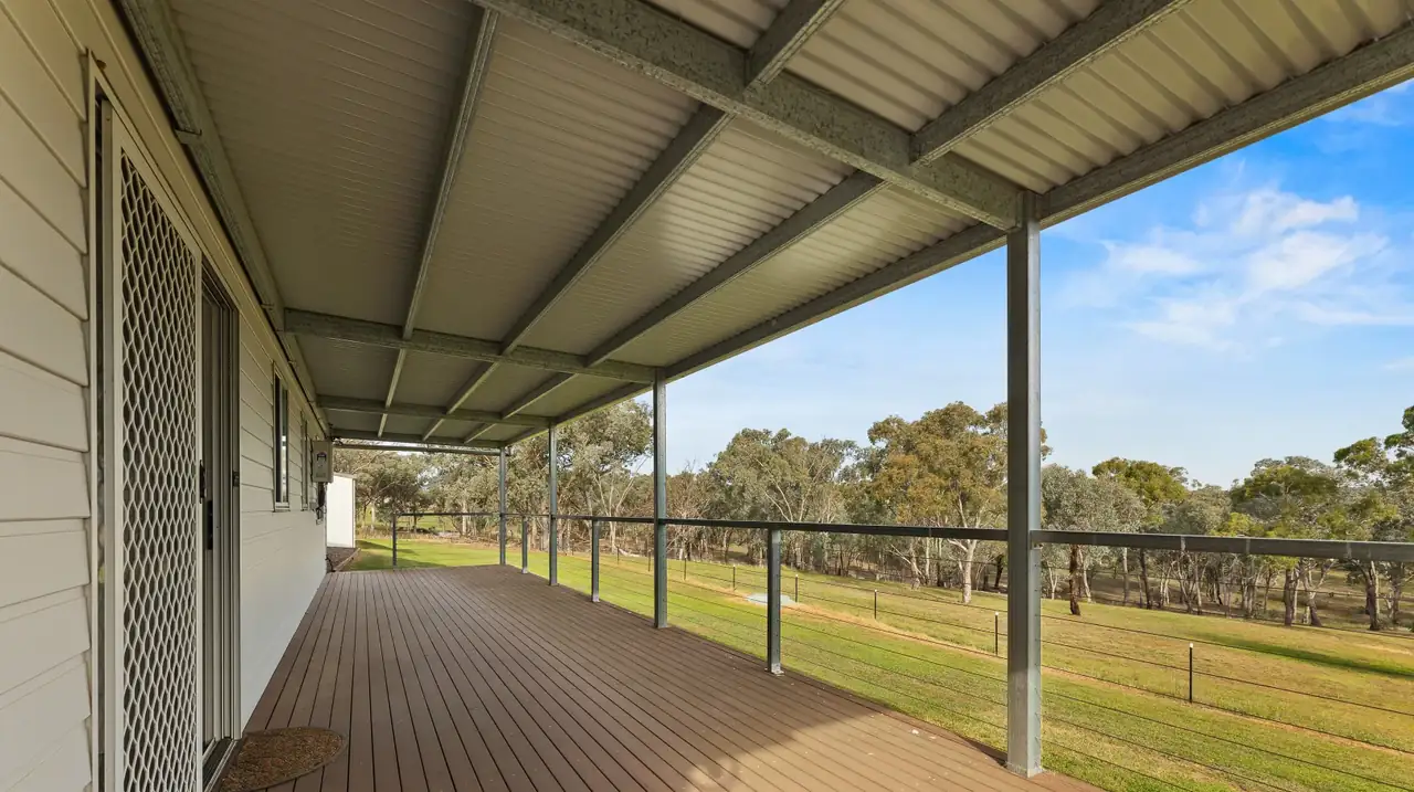 The long covered verandah with wire balustrade, looking out over mown lawn and gum trees